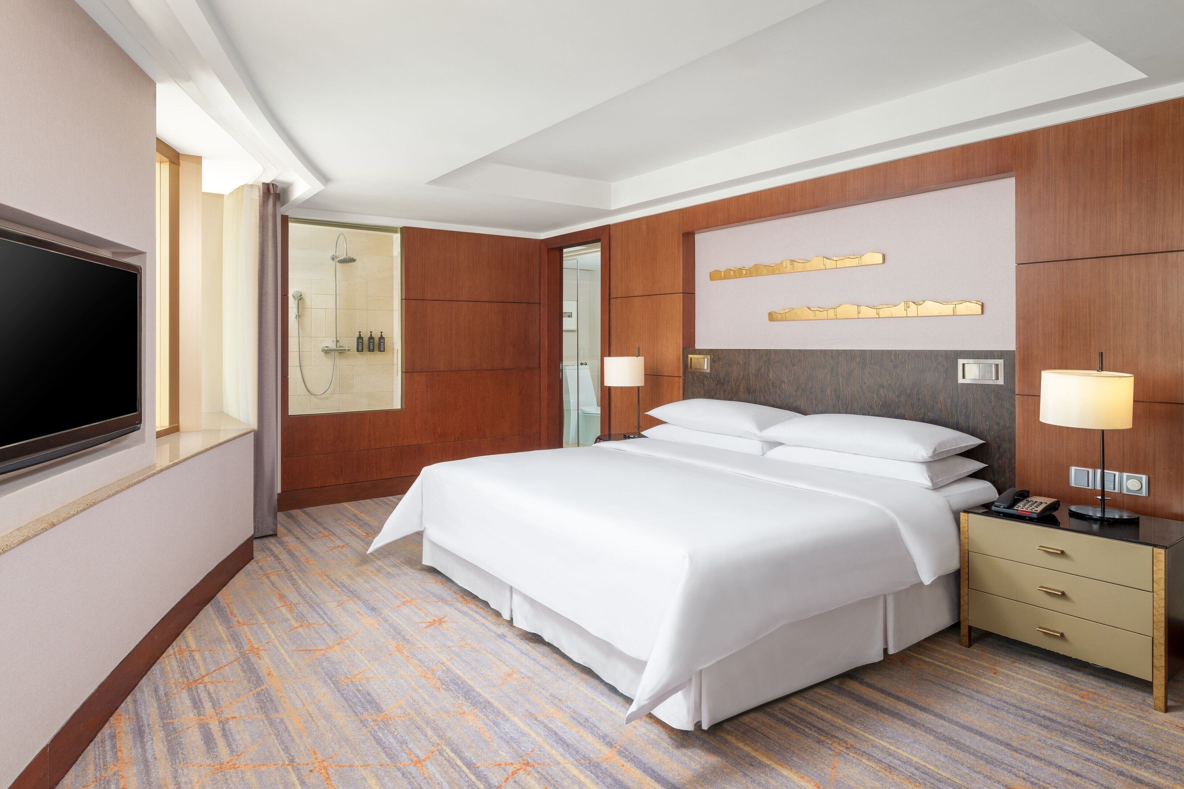 Habitación de hotel con una cama grande, televisión, ducha y escritorio con lámpara.
