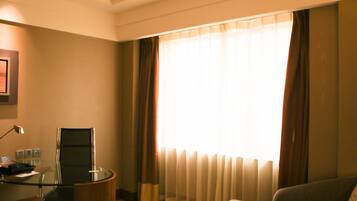 A hotel room with a glass desk, a chair, a sofa, and a large window with curtains.