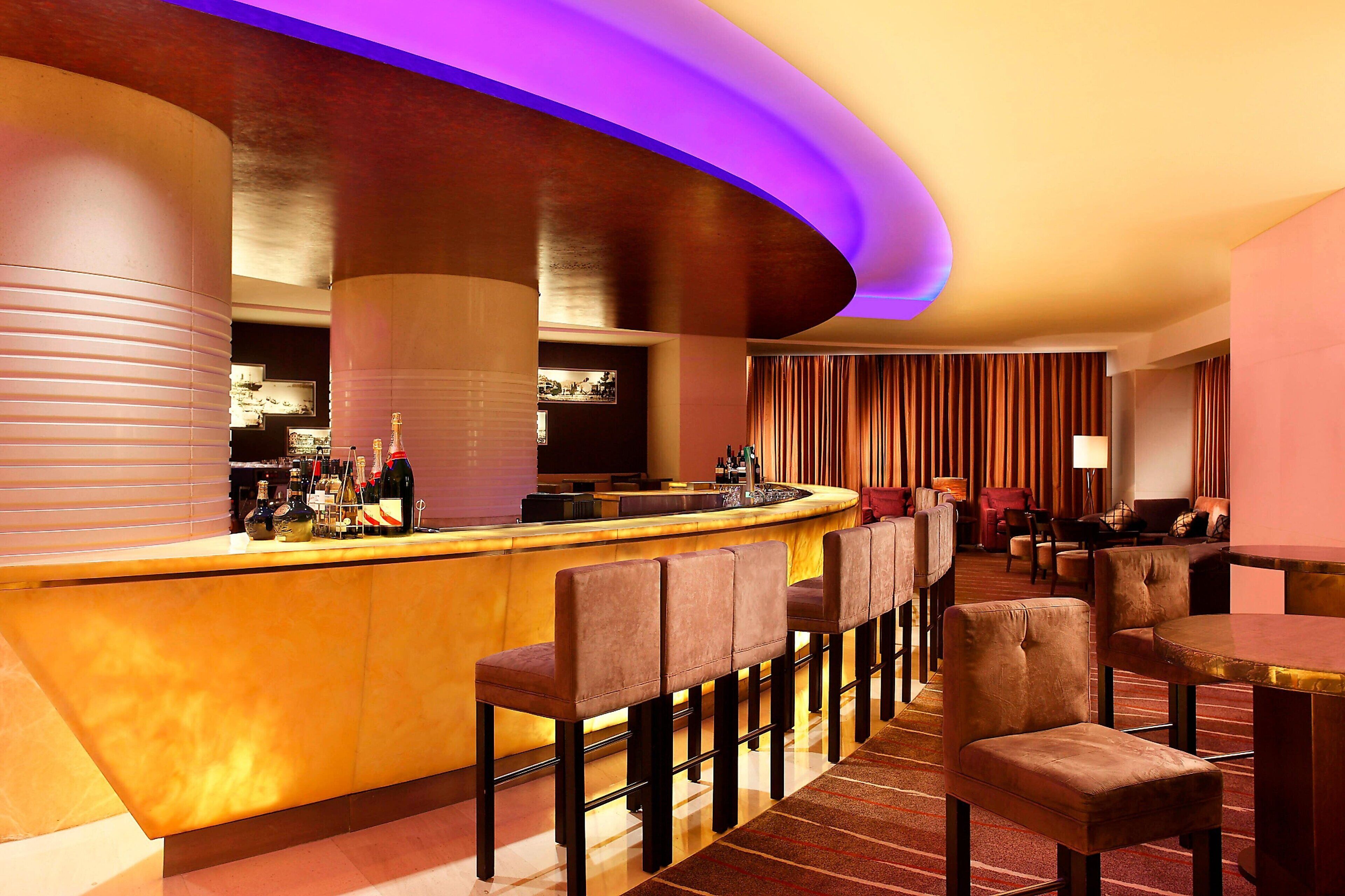 A bar area with a curved counter, multiple bar stools, and a seating area with tables and chairs.