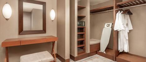 A hotel room with a wooden desk, bench, wardrobe, and a mirror.