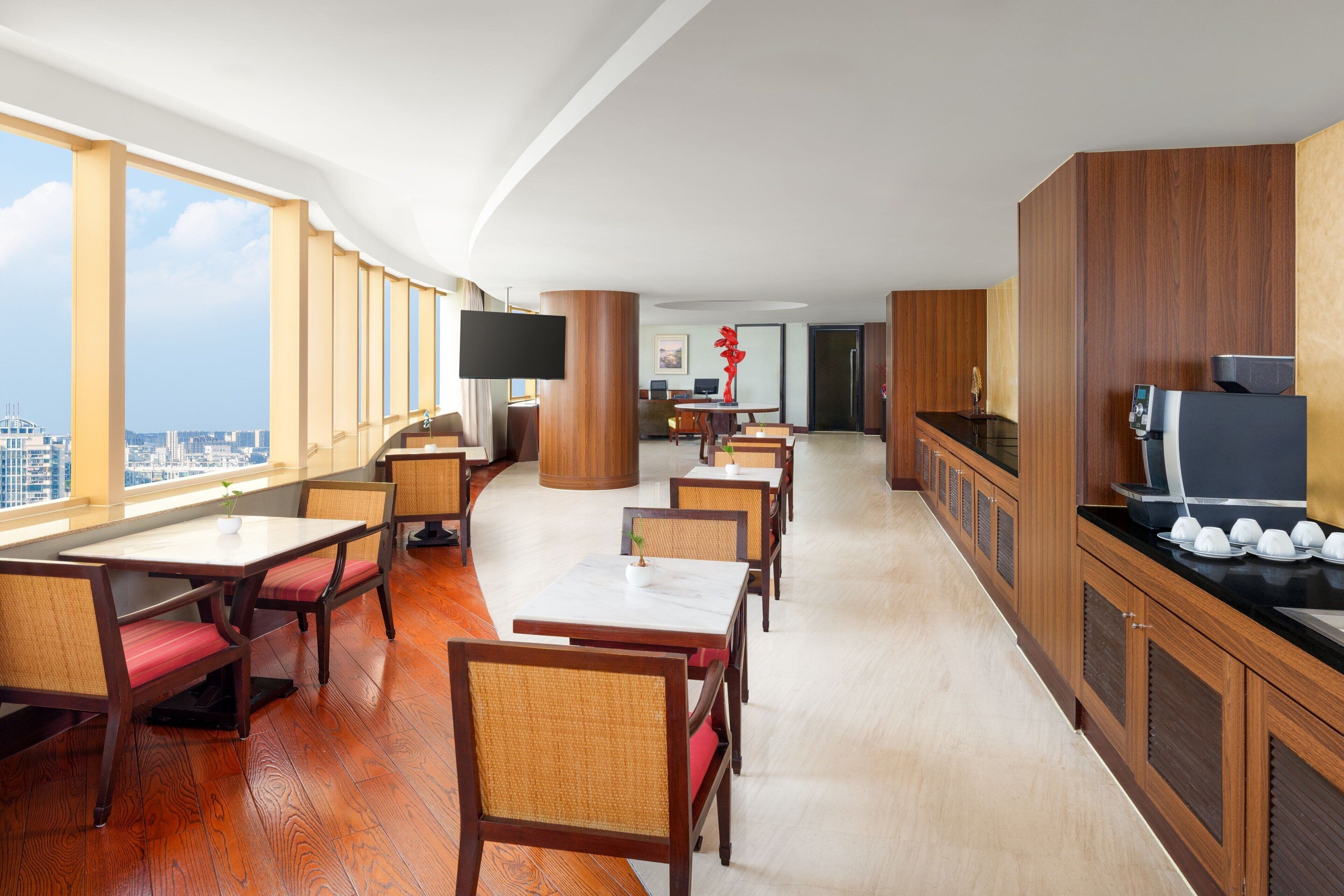 A hotel dining area with wooden tables and chairs, a flat-screen TV, and a city view.