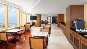 A hotel dining area with wooden tables and chairs, a flat-screen TV, and a city view.
