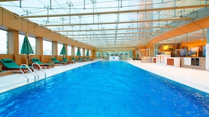 Una piscina interior con techos de vidrio transparente, múltiples sillones de descanso y una zona de recepción.