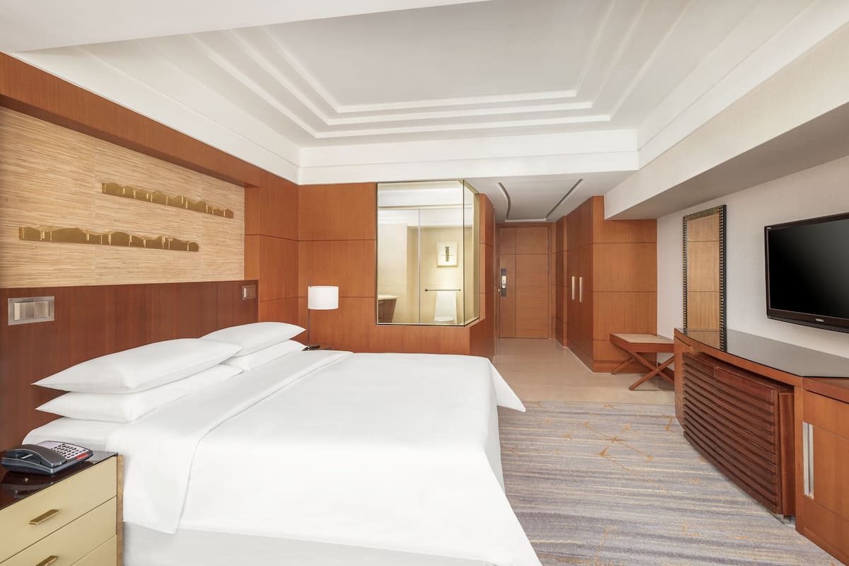 A hotel room with a large bed, a television, a mirror, and a desk with a chair.