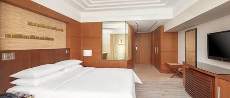 Habitación de hotel con una cama grande, televisor, espejo y escritorio con silla.