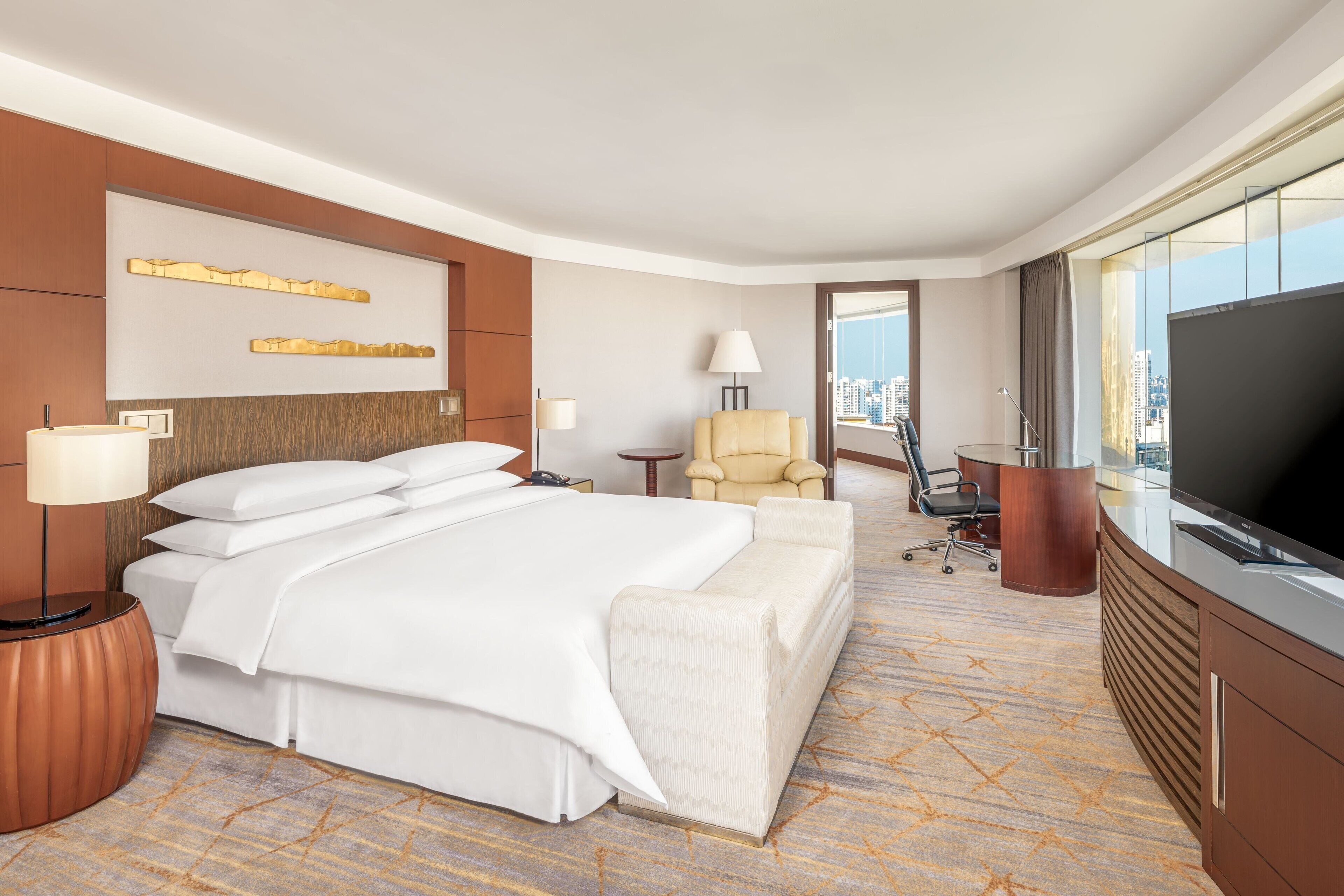 A hotel room with a large bed, a TV, a desk, and a chair.