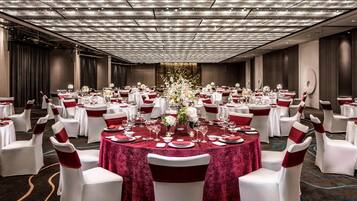 A banquet hall with round tables, white chairs, and red accents.