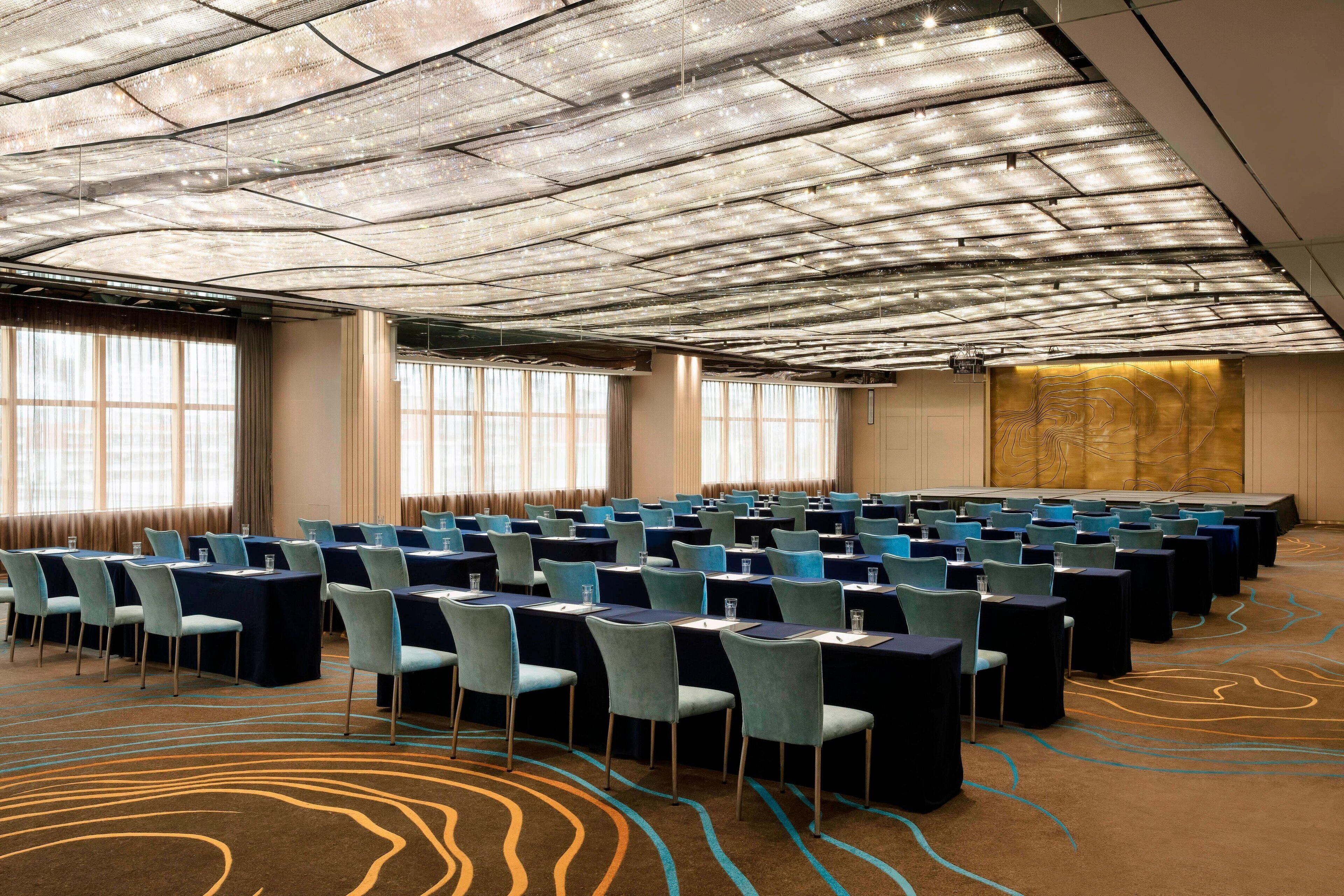 A conference room with rows of tables and chairs, large windows, and a patterned carpet.