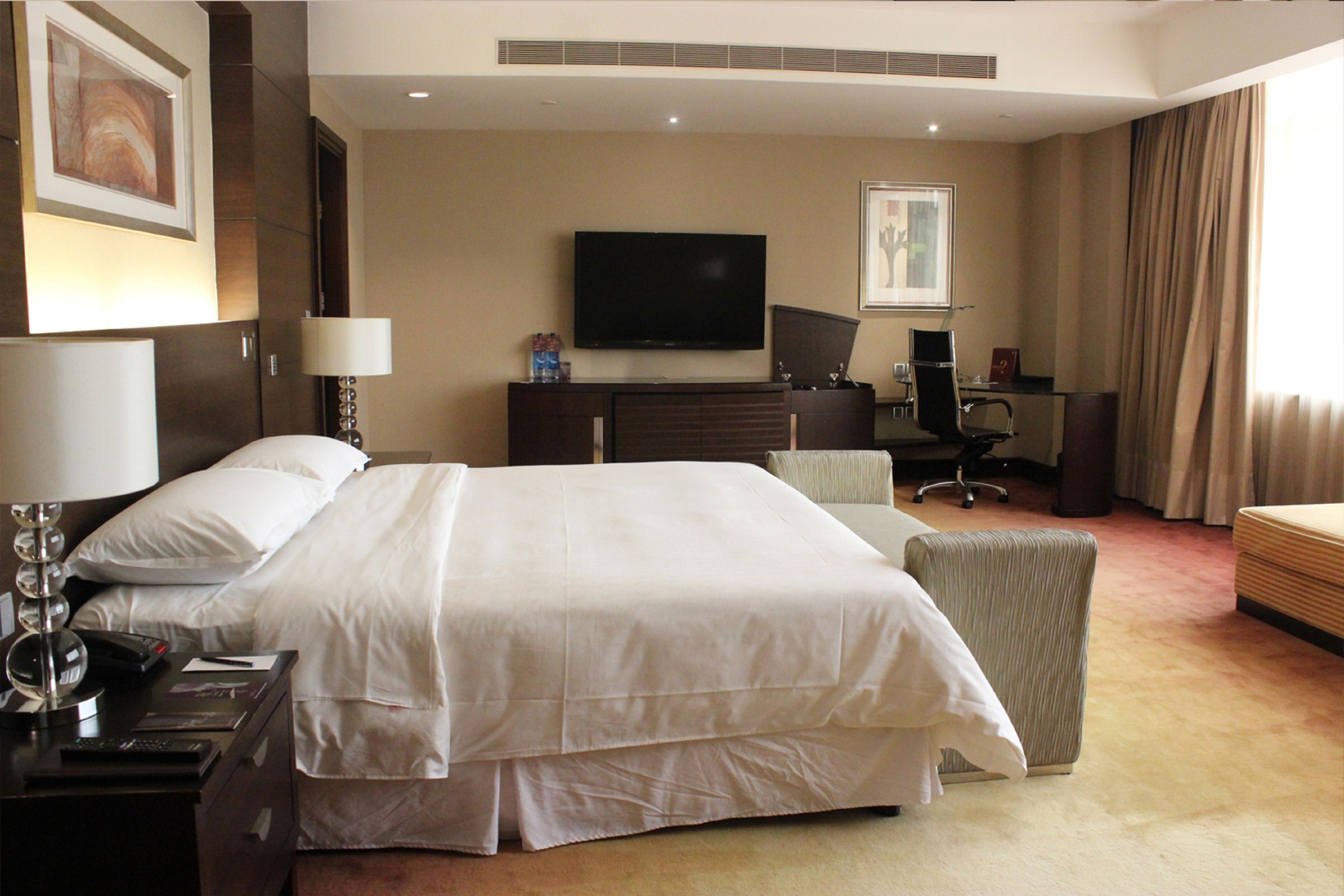 A hotel room with a large bed, a desk with a computer, a TV, and a chair.
