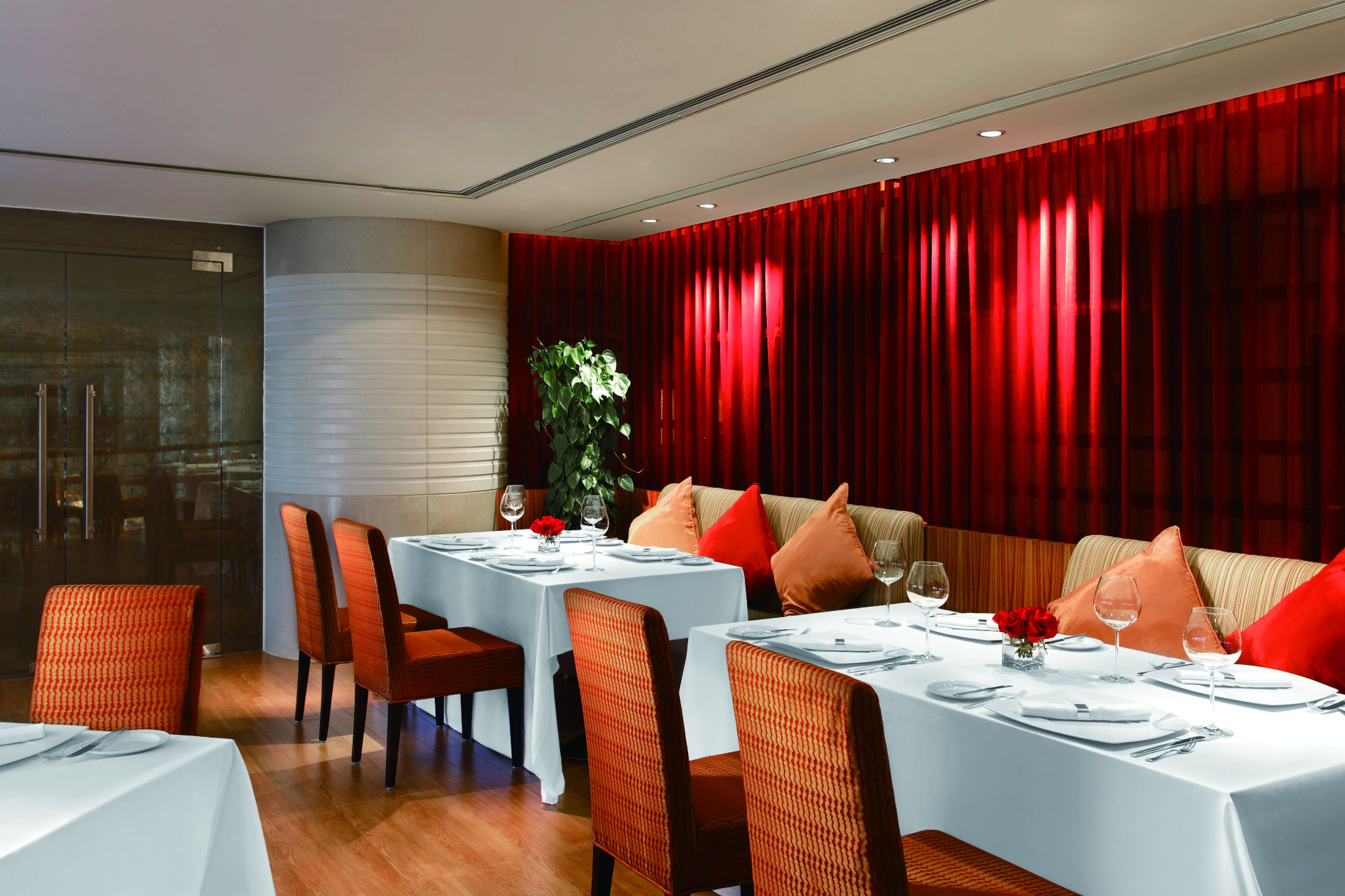 Un restaurante con mesas dispuestas para comer, cortinas rojas y una planta en la esquina.