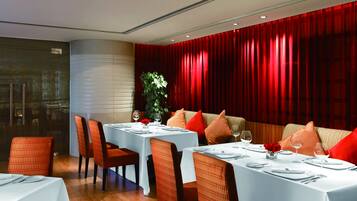 Un restaurante con mesas dispuestas para comer, cortinas rojas y una planta en la esquina.