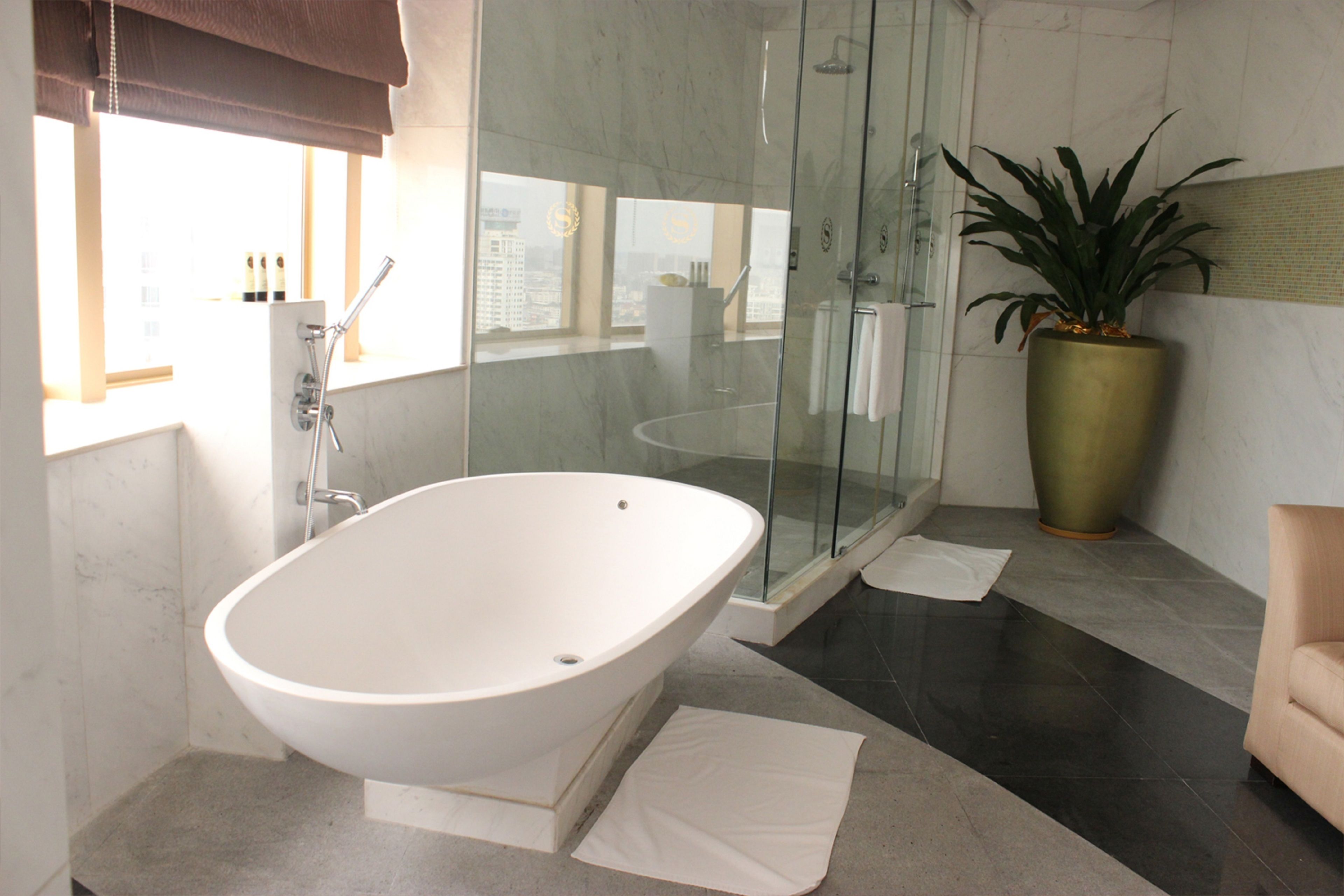 A modern bathroom with a freestanding bathtub, a glass-enclosed shower, and a potted plant.