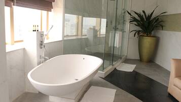 A modern bathroom with a freestanding bathtub, a glass-enclosed shower, and a potted plant.