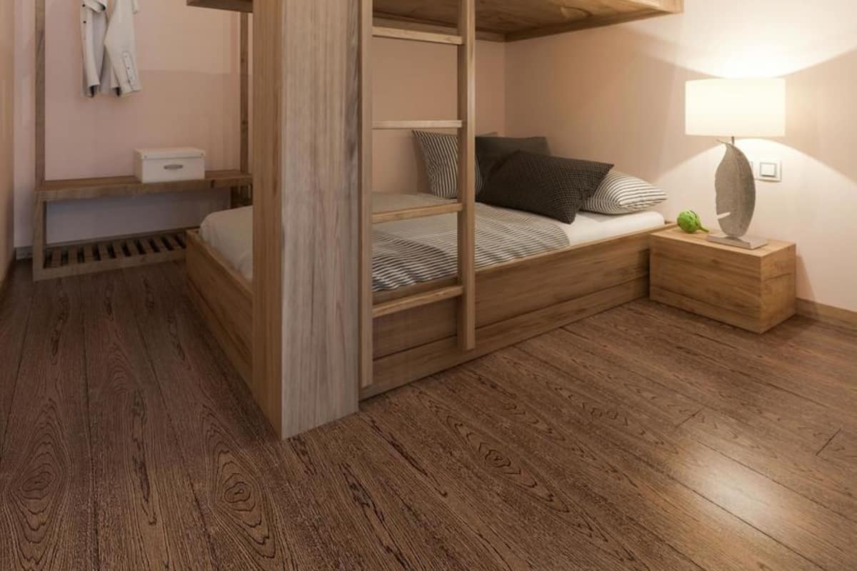 A bunk bed room with a wooden floor, a bedside table with a lamp, and a hanging coat rack.