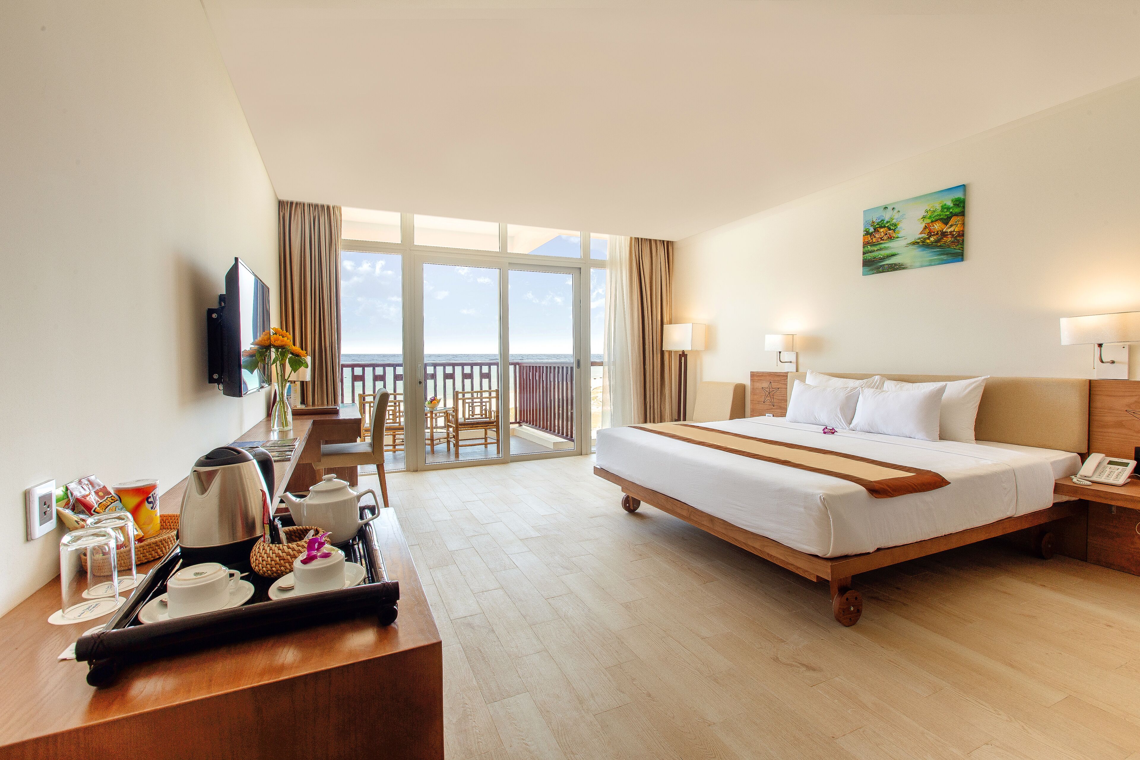 A hotel room with a bed, bedside table, a desk with a coffee maker, and a view of the outdoors.