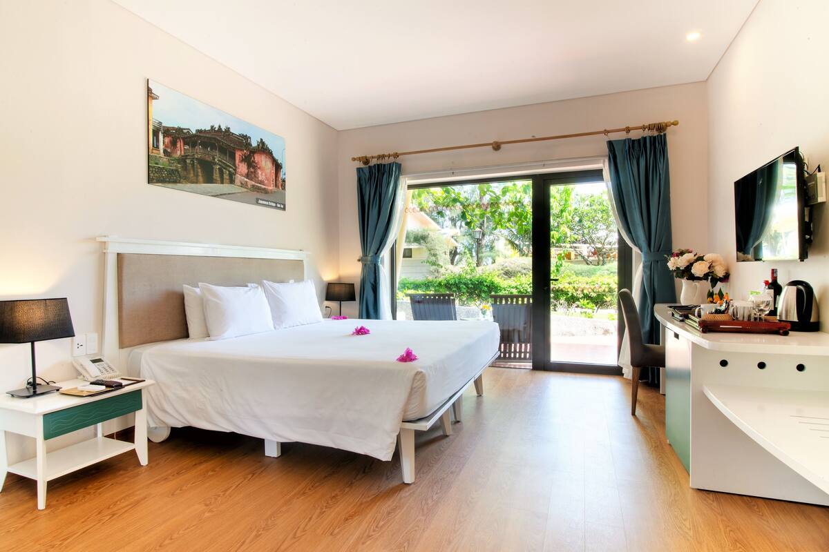 A hotel room with a bed, a desk, a chair, a TV, and a view of the outdoors.