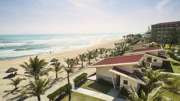 Un hotel frente a la playa con varias habitaciones, una playa de arena y palmeras.