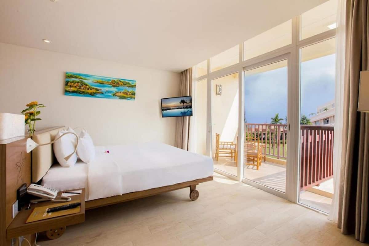 A hotel room with a bed, a desk with a lamp, a TV, and a painting on the wall.