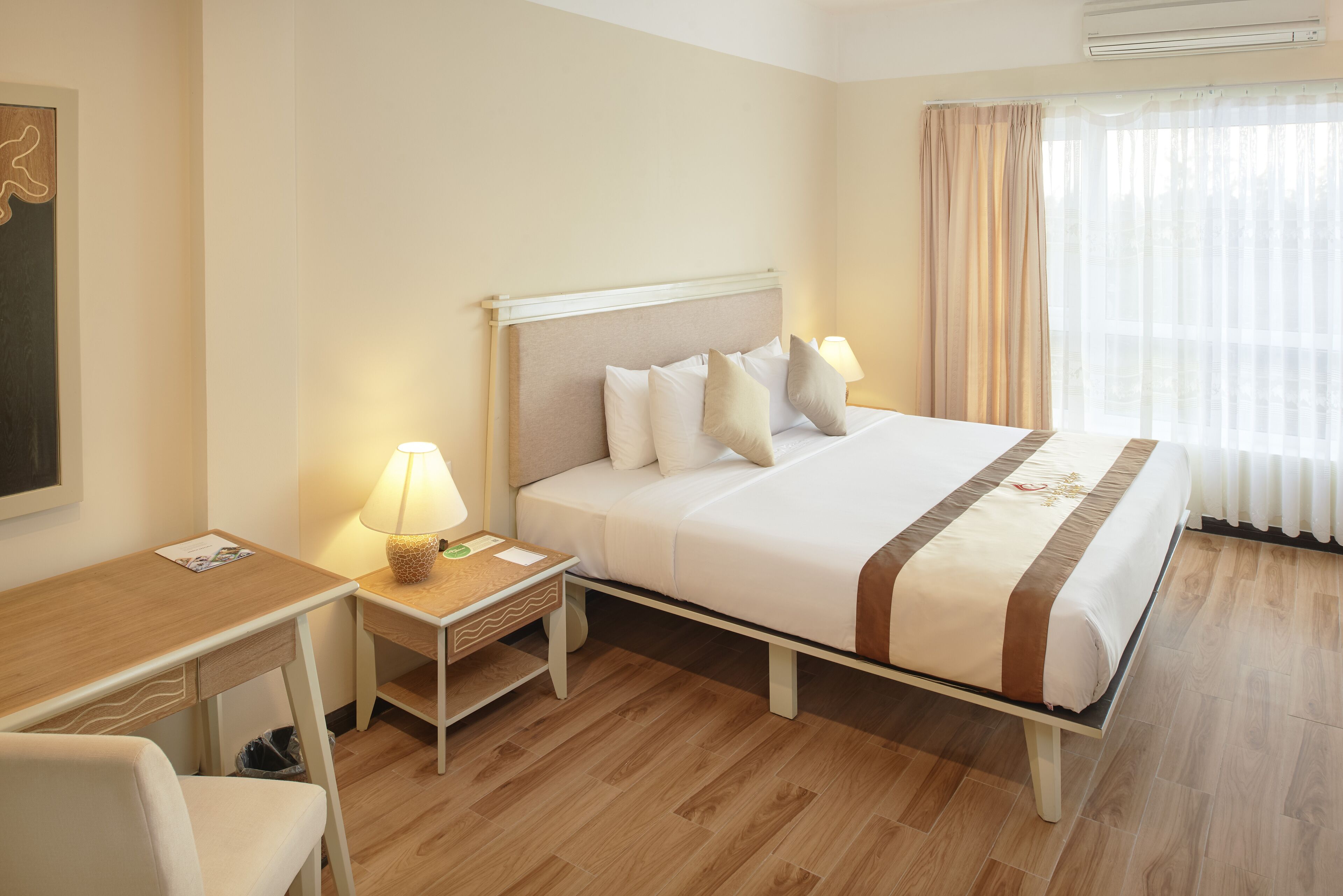 A hotel room with a bed, bedside table, lamp, and a desk with a chair.