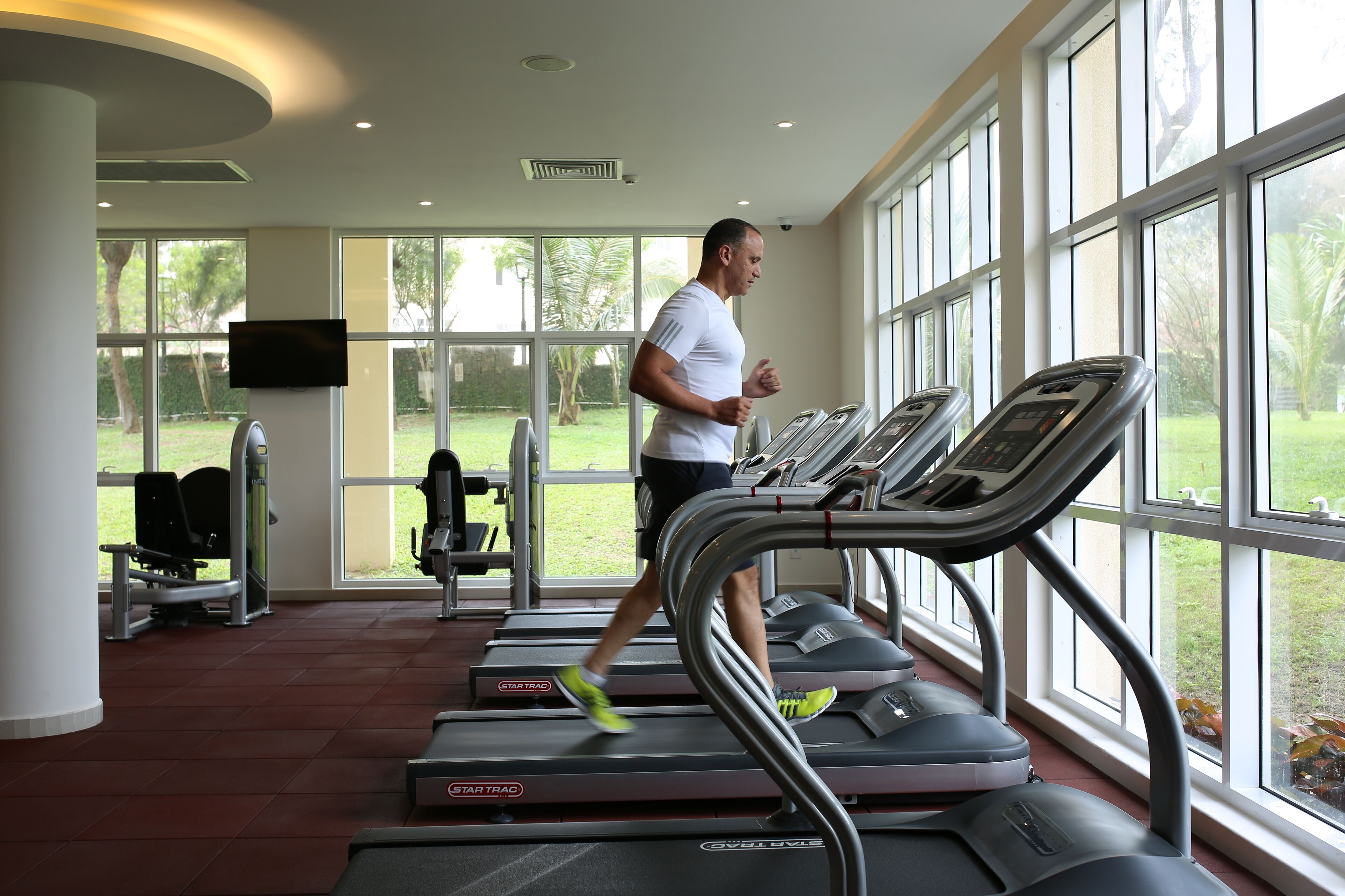 Un gimnasio con cintas de correr, equipo de ejercicio y amplias ventanas con vistas al exterior.