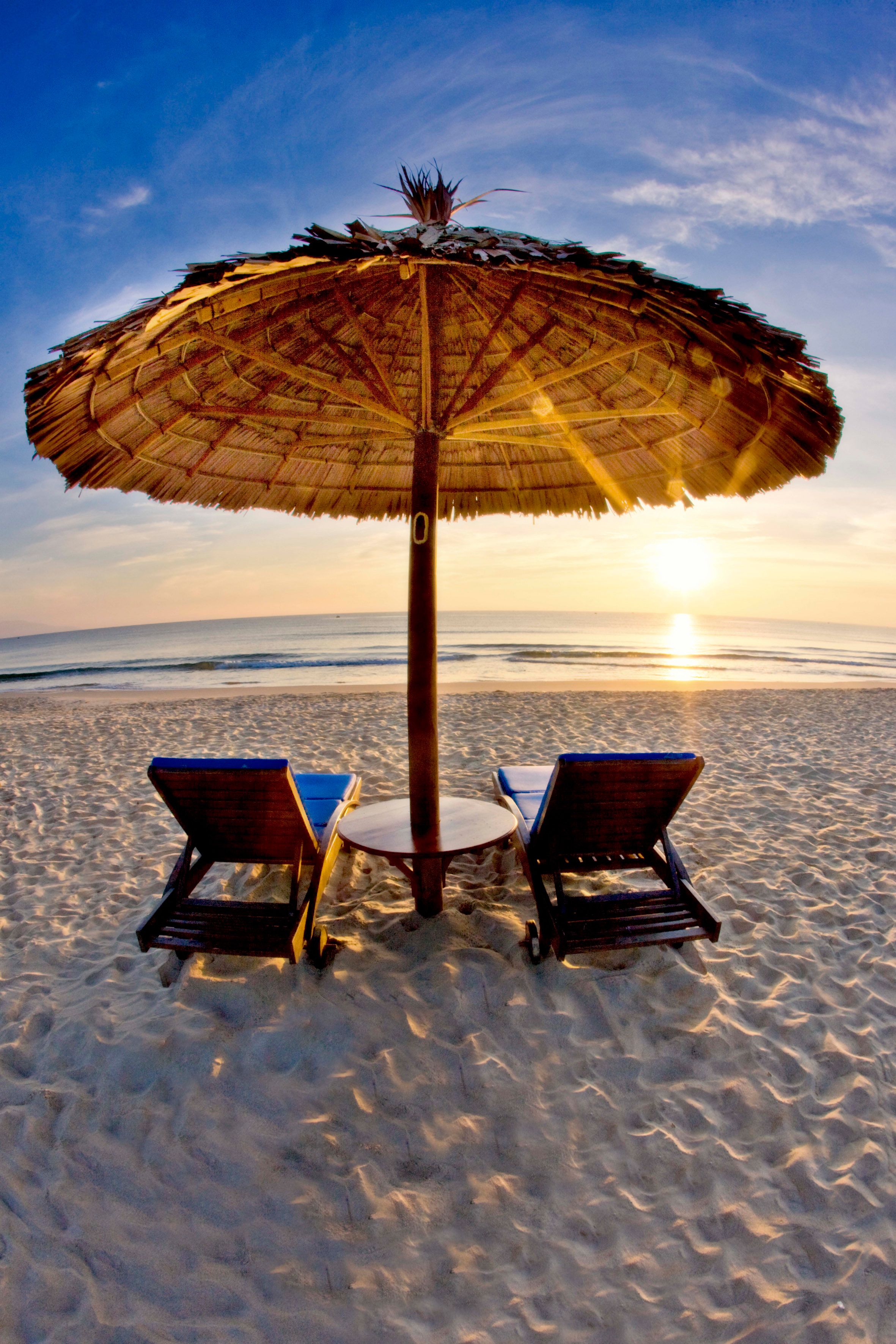 A beach scene with a thatched umbrella, two lounge chairs, and a small table.