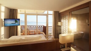 A hotel room with a bed, a TV, a balcony with a view of the sea, and a bathroom with a bathtub.