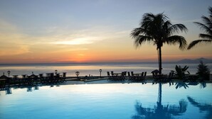 A poolside area with lounge chairs and a palm tree, overlooking a sunset over the ocean. - Sandy Beach Non Nuoc Resort (Da Nang)