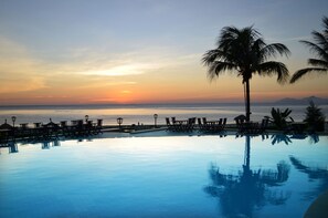A poolside area with lounge chairs and a palm tree, overlooking a sunset over the ocean. - Sandy Beach Non Nuoc Resort (Da Nang)