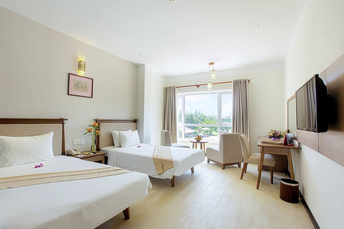 A hotel room with two beds, a desk, a chair, a TV, and a window with curtains.