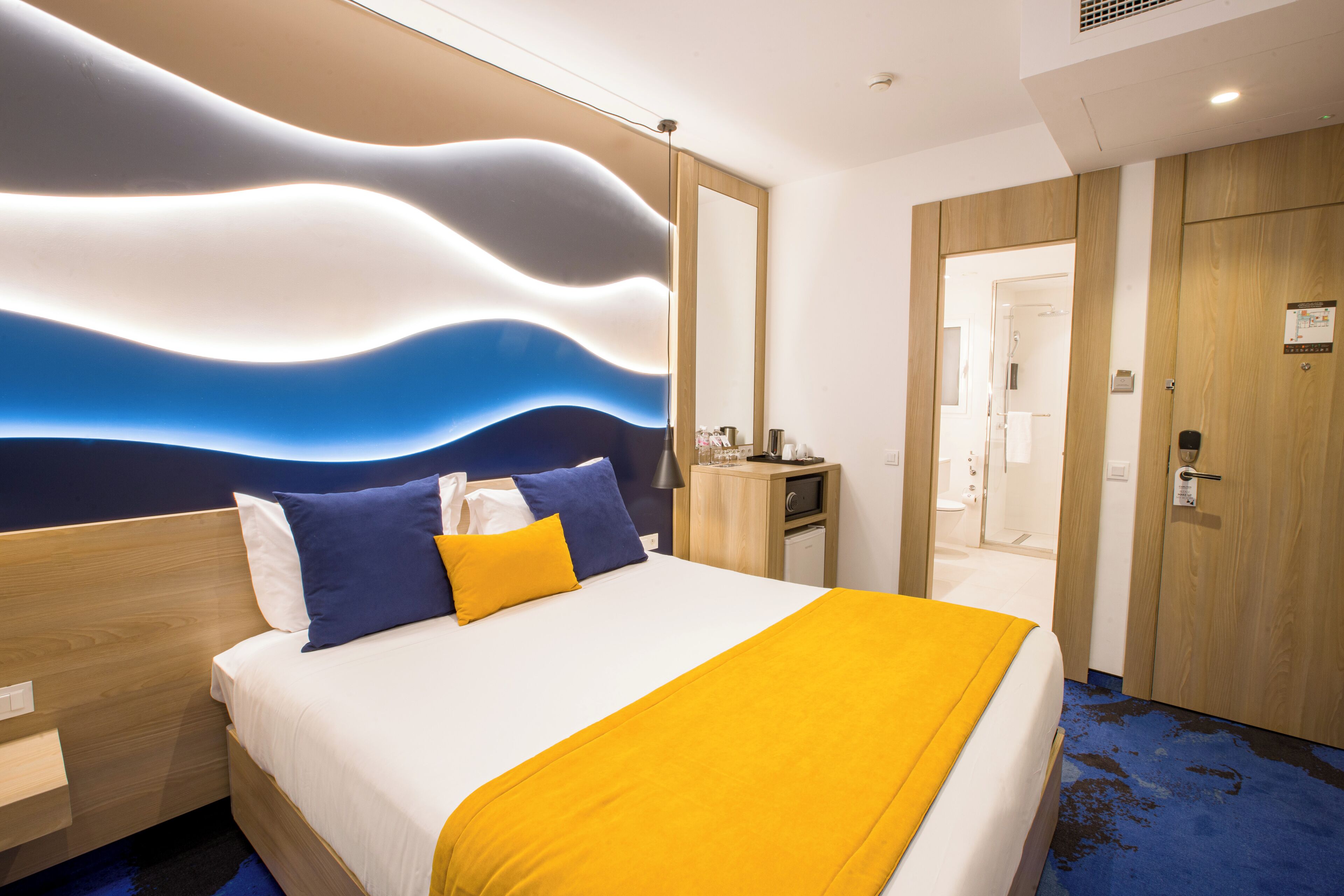 Habitación de hotel con cama, mesita de noche y una pared con diseño ondulado.