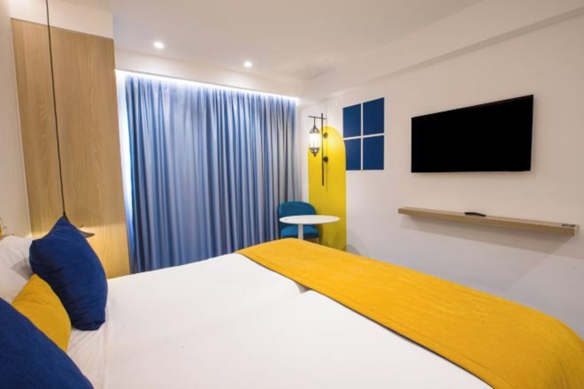 Habitación de hotel con cama, televisión, escritorio y ventana con cortinas.