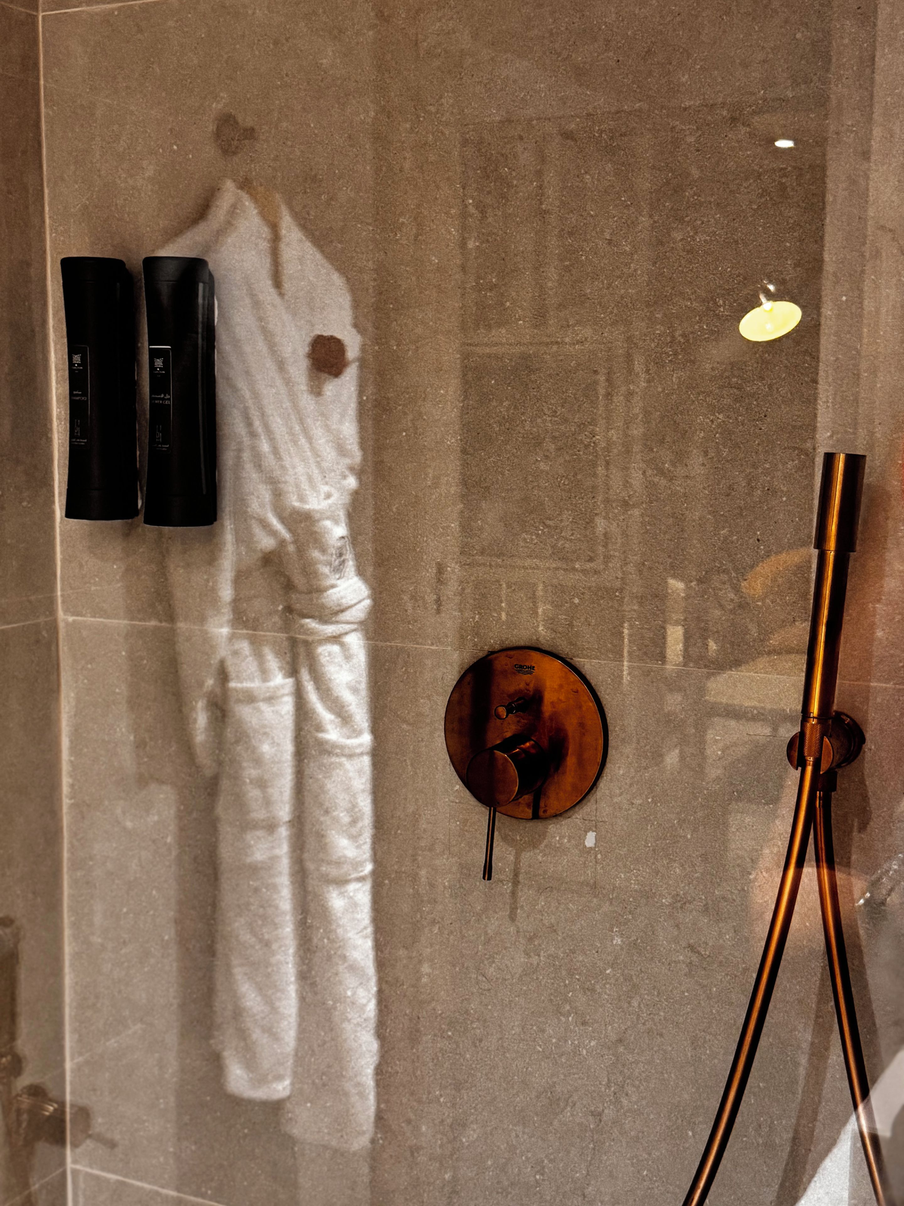 Een badkamer met een glazen douchecabine, een handdoekhouder met een witte handdoek en een zwart object aan de muur.
