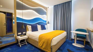 Ein modernes Hotelzimmer mit einem großen Bett, einem Nachttisch, einem kleinen Tisch, einem Sessel und einer Wand mit einem gewellten Muster.