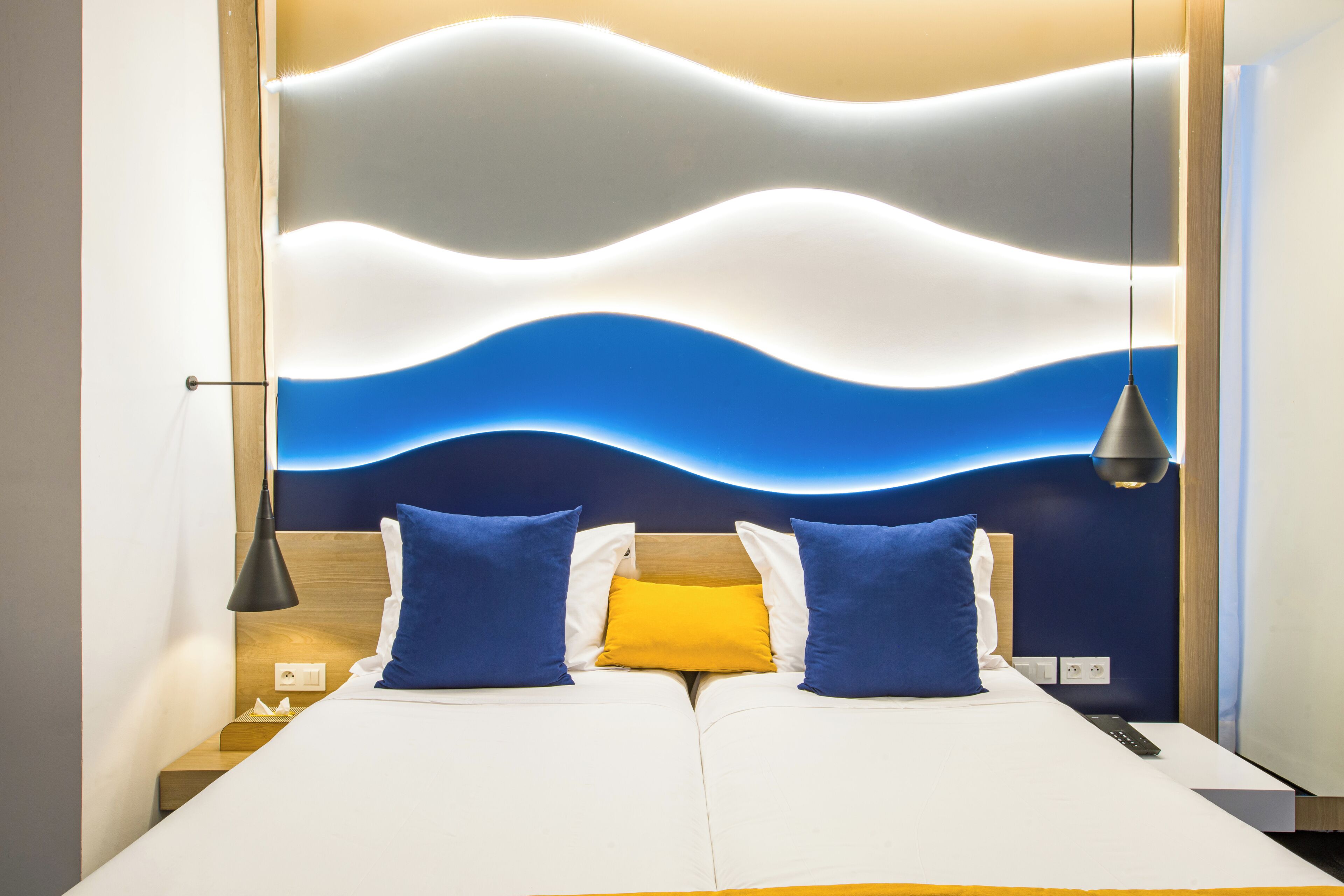 Habitación de hotel con cama, mesita de noche, lámpara y un muro con diseño ondulado.