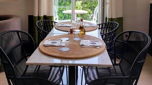 Comedor con una mesa dispuesta para cuatro personas, sillas negras y vistas a edificios y follaje por un amplio ventanal.