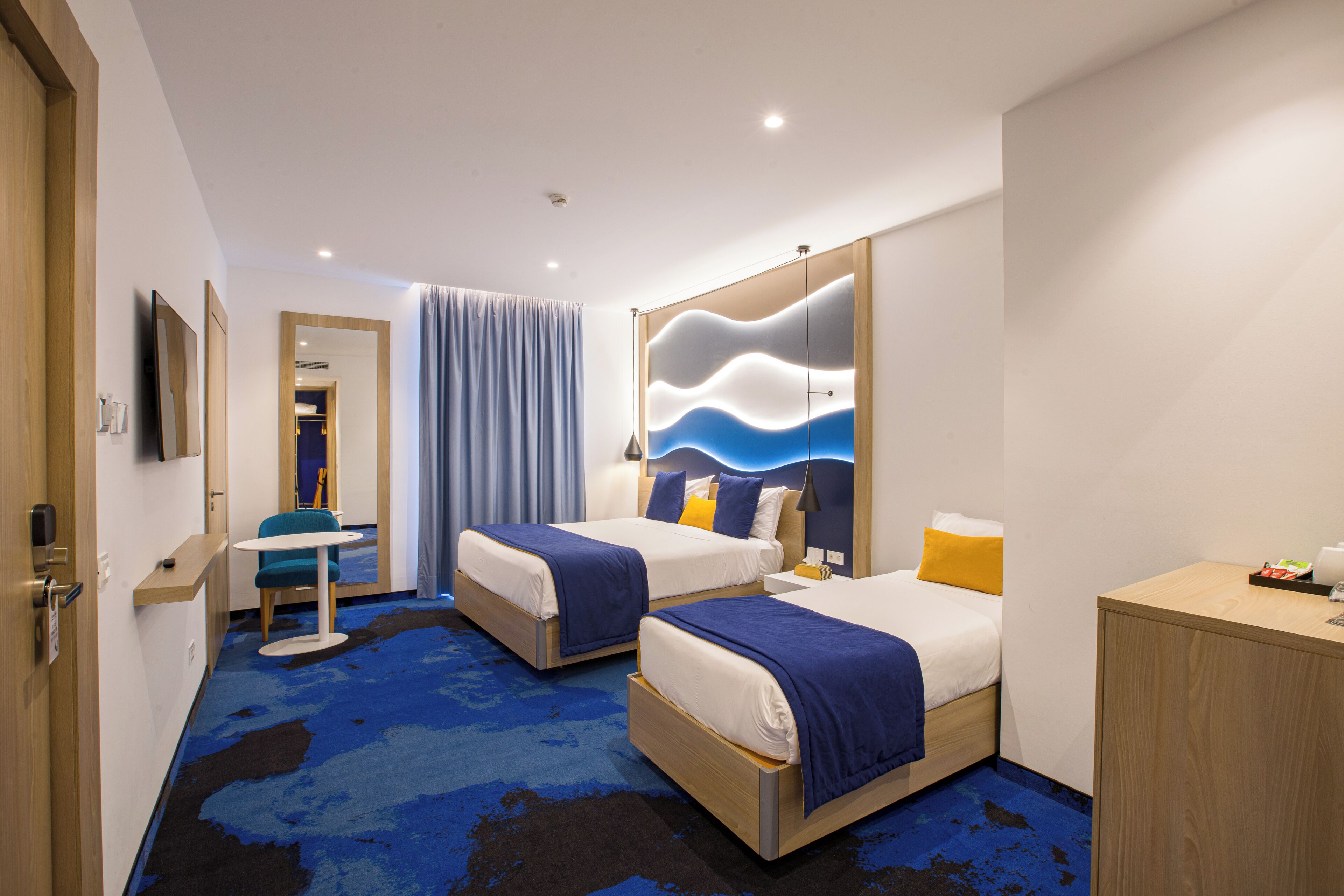 Una habitación de hotel con dos camas, un escritorio, una silla, un espejo y un armario.