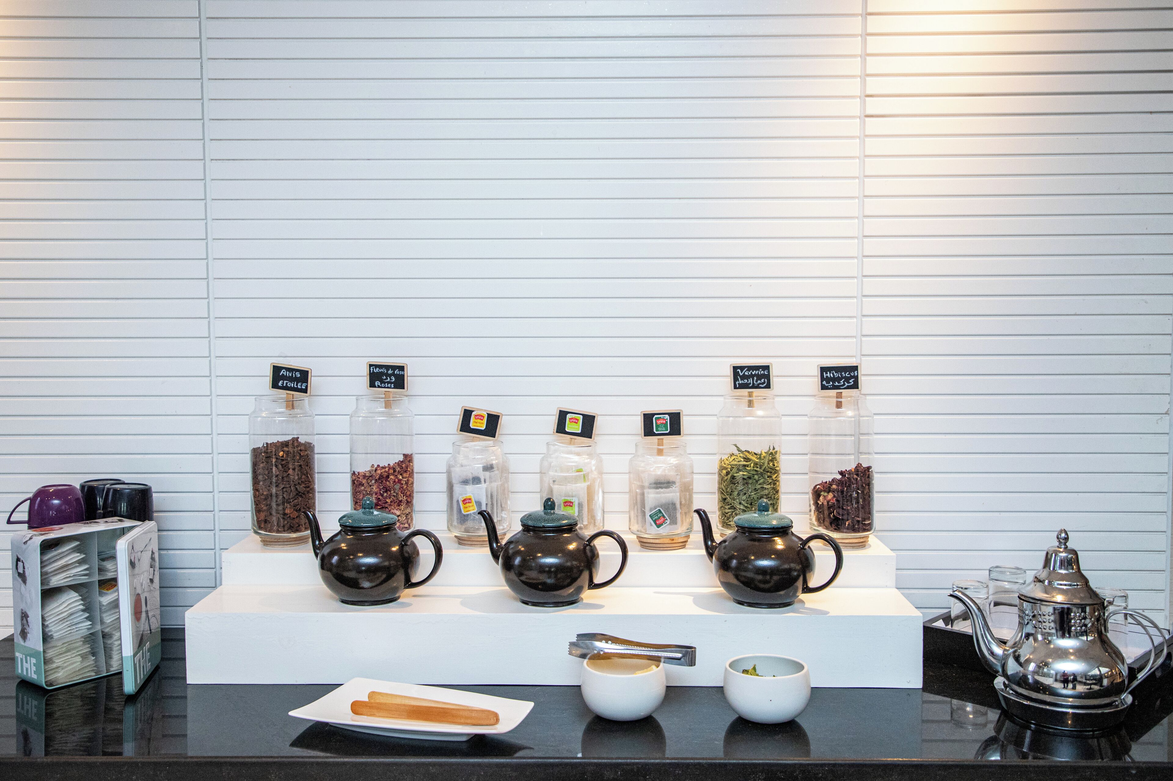 Una exposición de teteras y recipientes para té sobre una encimera con un fondo de pared de azulejos blancos.