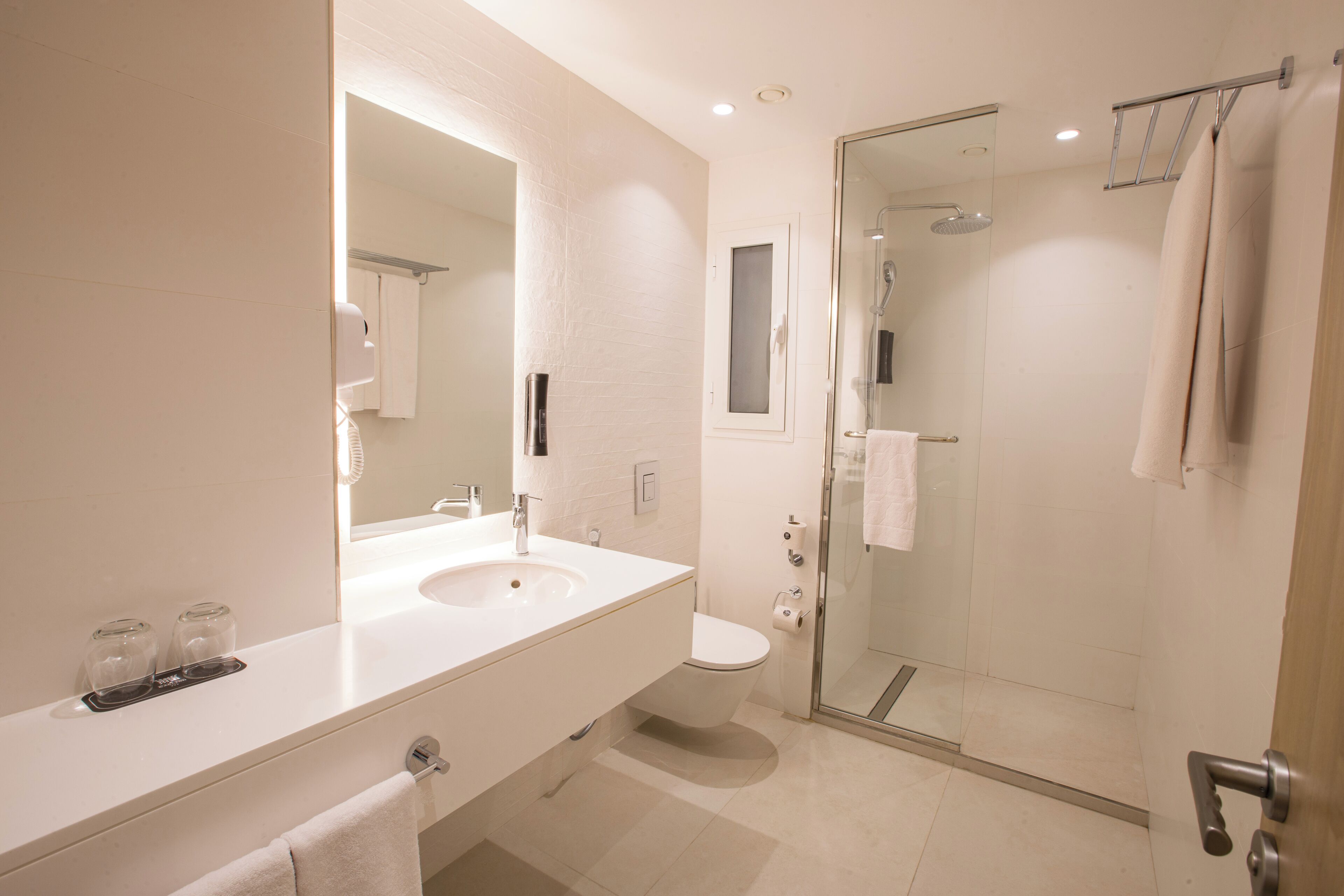 Un baño moderno con un espejo grande, un lavabo, un inodoro y una zona de ducha con mampara de cristal.