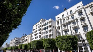 Una calle bordeada de edificios de varios pisos, árboles y peatones.