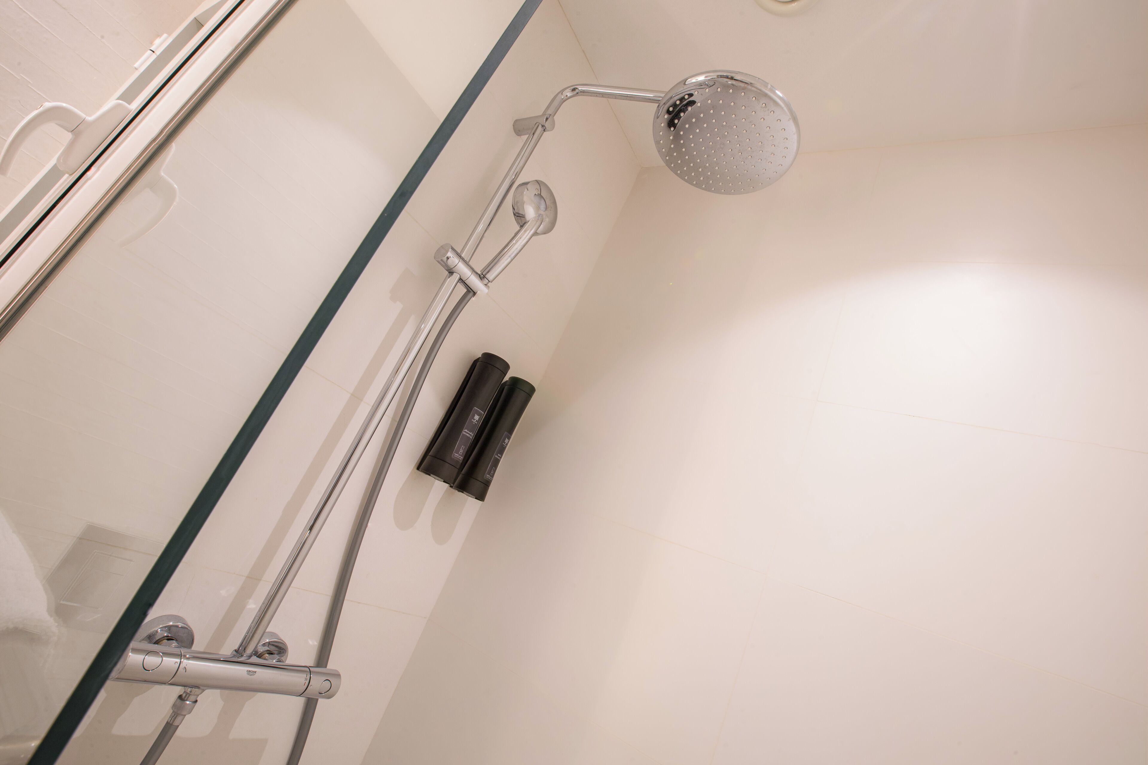 Une douche équipée d’un pommeau de douche à main, d’un appareil de massage à main et d’un panneau de commande fixé au mur.