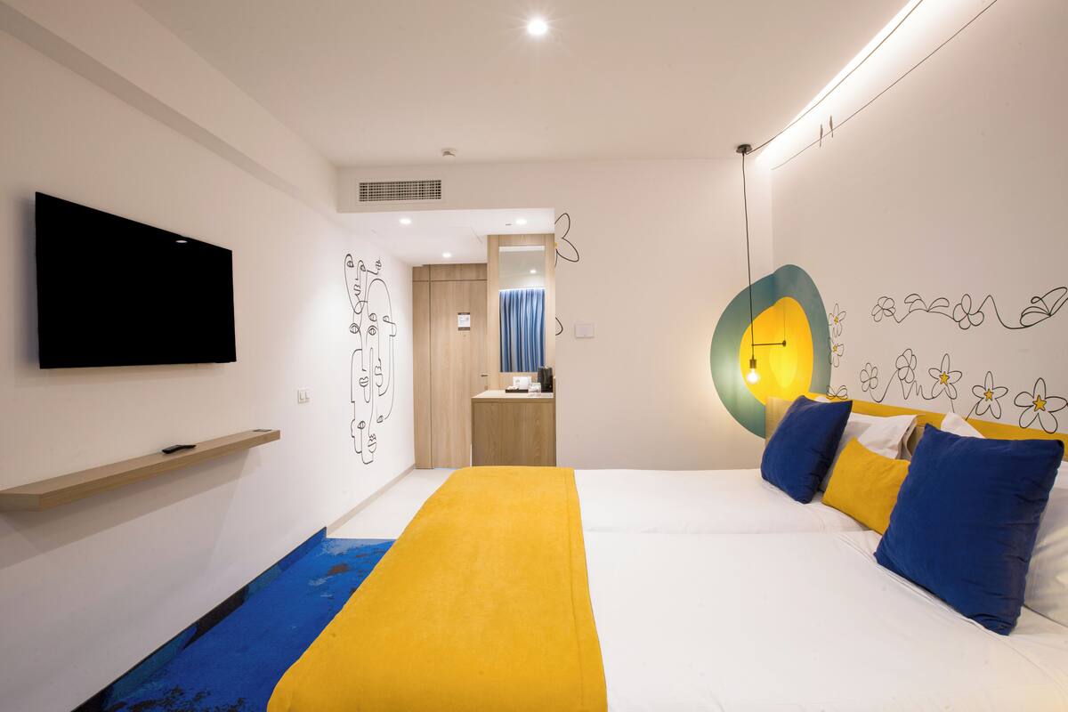 A modern hotel room with a bed, a flat-screen TV, a wooden shelf, and a bathroom visible through an open door.