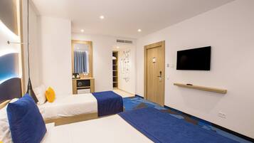 A hotel room with two beds, a TV, a wardrobe, and a bathroom visible through an open door.