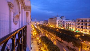 Una calle urbana al anochecer con edificios a ambos lados, cielo despejado y una acera para peatones.