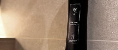 A black cylindrical container labeled 'CARLTON LIQUID SOAP' with instructions to 'press the bottle' on a beige tiled wall.