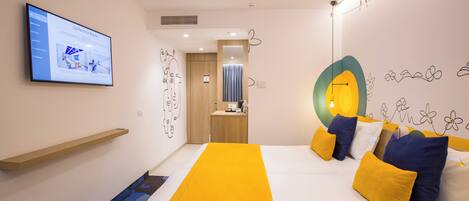 Una habitación de hotel moderna con una cama grande, un televisor en la pared y una pequeña zona de escritorio.