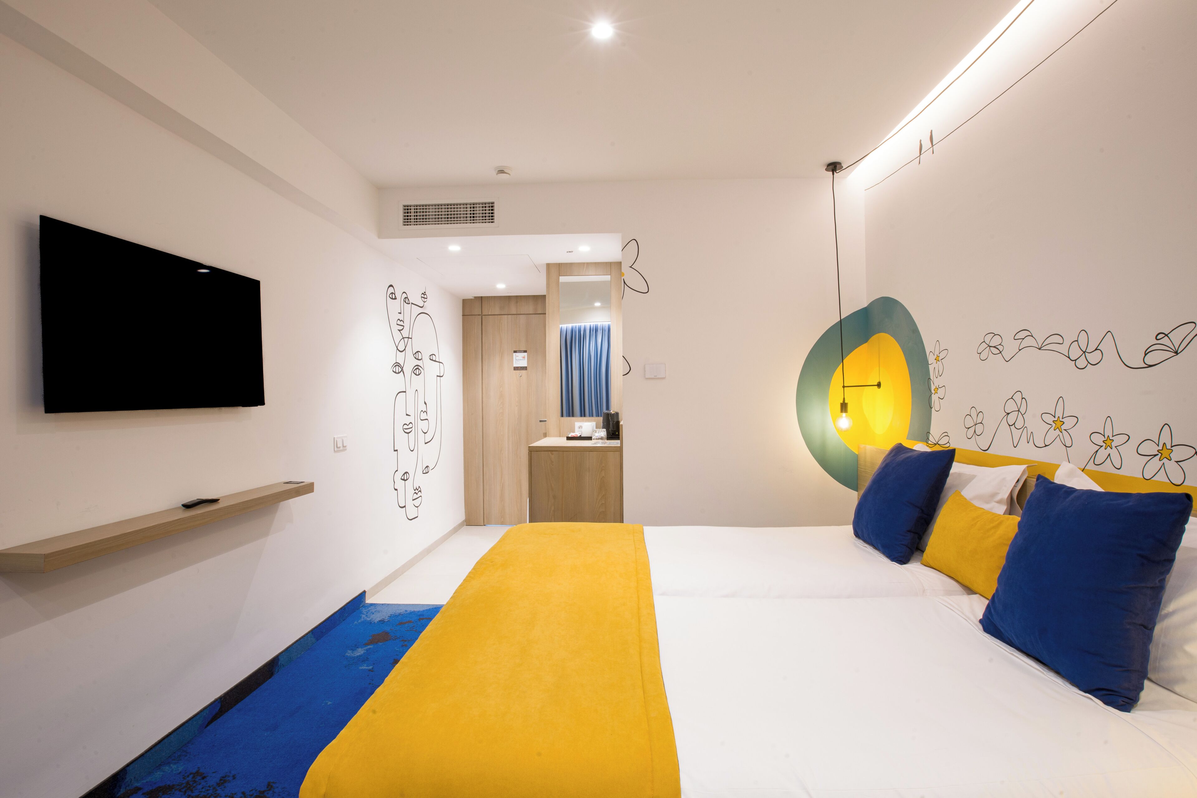 Een moderne hotelkamer met een bed, een flatscreen televisie, een houten plank en een badkamer zichtbaar door een geopende deur.