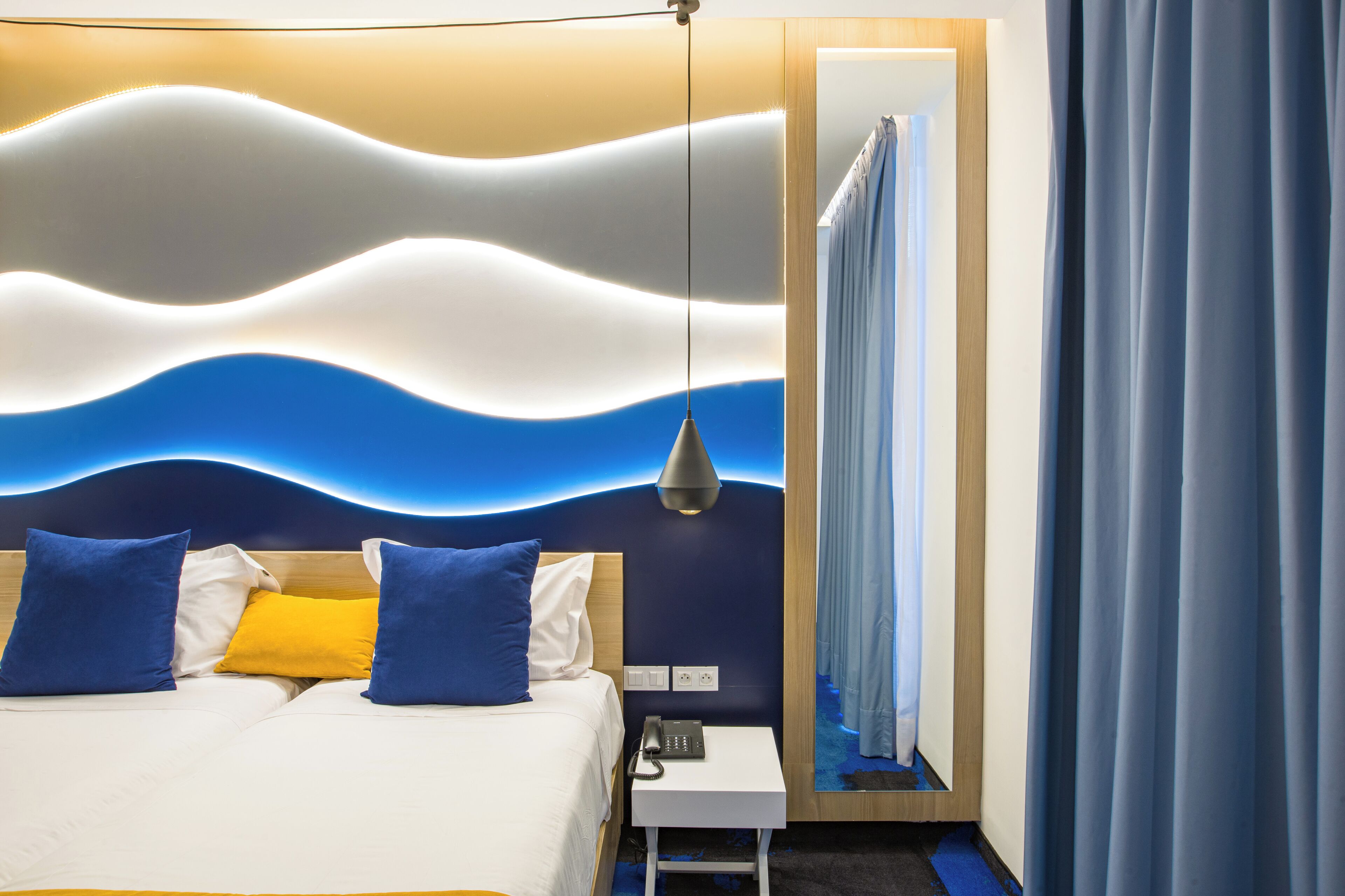 A hotel room with a bed, bedside table, and a wall with a wavy design.