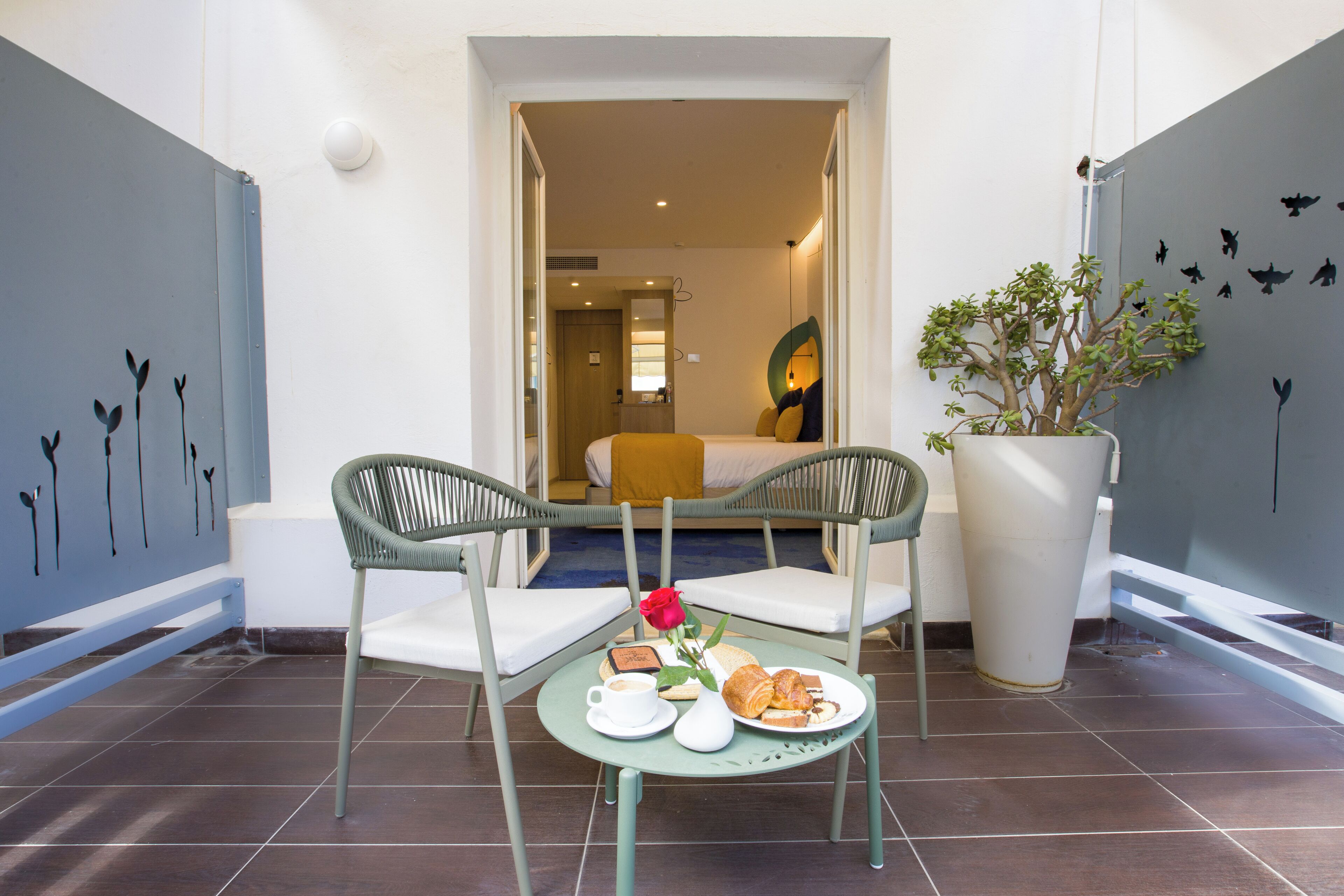 A dining area with a table set for two, a potted plant, and a view into the room.