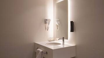 Un baño moderno con un lavabo blanco, un espejo, un perchero para toallas y un secador de pelo fijado a la pared.