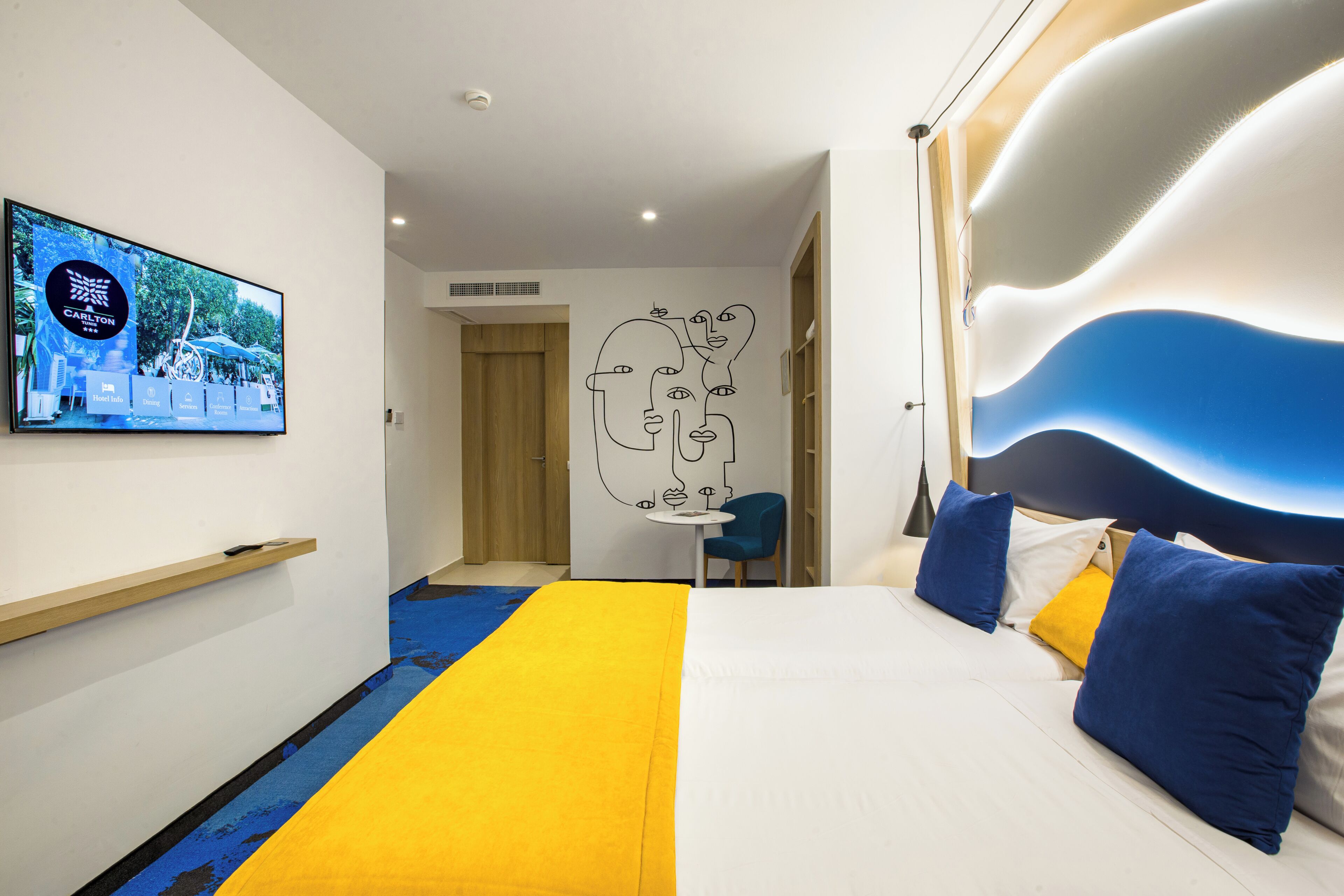 A hotel room with a bed, a TV on the wall, a desk, and a chair.